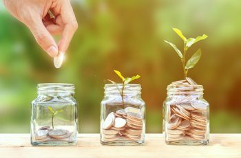 Money savings, investment, making money for future, financial wealth management concept. A man hand holding coin over stacked coins in glass jar and growing tree plant depicts Fund growth and wealth.